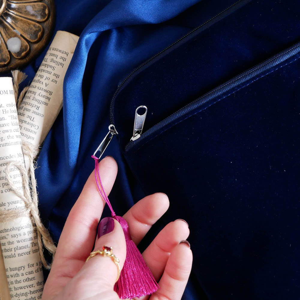The reverse of the Blue Serpents & Swords E-Reader Sleeve. On a blue fabric background, a hand shows the pink satin interior against the delicate velvet finishing of the sleeve next to some paper scrolls.