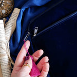 The reverse of the Blue Serpents & Swords E-Reader Sleeve. On a blue fabric background, a hand shows the pink satin interior against the delicate velvet finishing of the sleeve next to some paper scrolls.