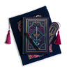 The journal bundle from the Serpents & Swords collection. This navy blue variation includes a book sleeve, journal, pen and bookmark from the collection. All feature a design with motifs of crowns swords and snakes in shades of bright pink, gold, and aqua. The journal, pen and bookmark feature gold foiling while the velvet book sleeve is embroidered. The sleeve and bookmark also feature bright pink tassels.