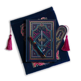 The journal bundle from the Serpents & Swords collection. This navy blue variation includes a book sleeve, journal, pen and bookmark from the collection. All feature a design with motifs of crowns swords and snakes in shades of bright pink, gold, and aqua. The journal, pen and bookmark feature gold foiling while the velvet book sleeve is embroidered. The sleeve and bookmark also feature bright pink tassels.