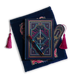 The journal bundle from the Serpents & Swords collection. This navy blue variation includes a book sleeve, journal, pen and bookmark from the collection. All feature a design with motifs of crowns swords and snakes in shades of bright pink, gold, and aqua. The journal, pen and bookmark feature gold foiling while the velvet book sleeve is embroidered. The sleeve and bookmark also feature bright pink tassels.