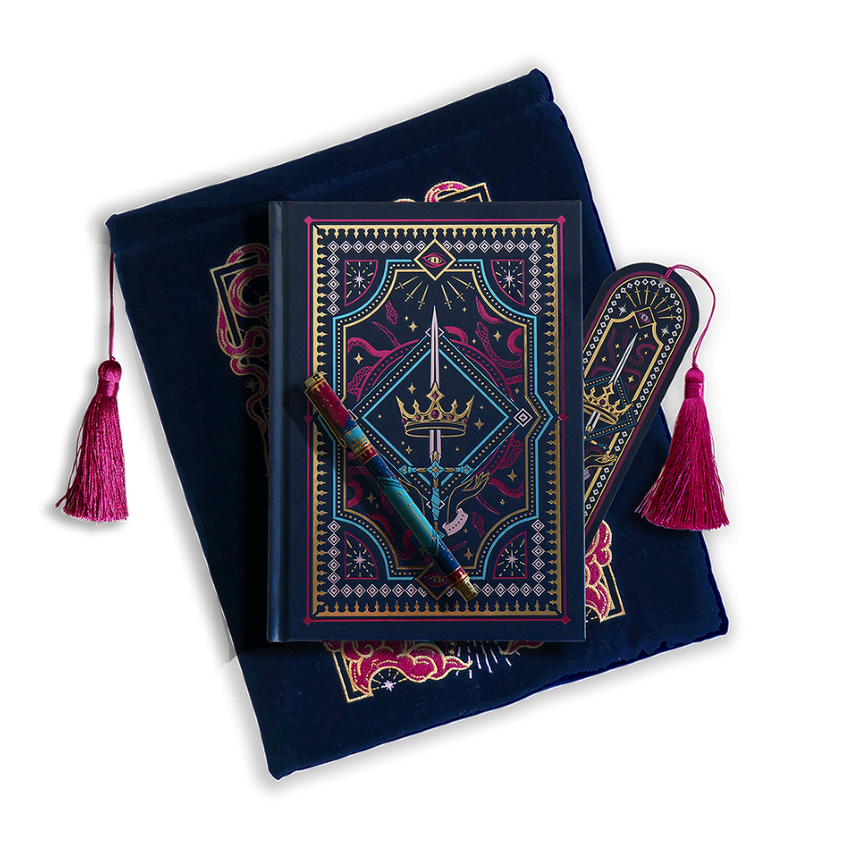 The journal bundle from the Serpents & Swords collection. This navy blue variation includes a book sleeve, journal, pen and bookmark from the collection. All feature a design with motifs of crowns swords and snakes in shades of bright pink, gold, and aqua. The journal, pen and bookmark feature gold foiling while the velvet book sleeve is embroidered. The sleeve and bookmark also feature bright pink tassels.