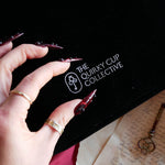 A close up of The Quirky Cup Collective logo on the black Serpents & Swords e-reader sleeve. The white logo features the key monogram