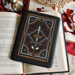 The Oath Breaker Kindle Sticker Insert by The Quirky Cup Collective shows in intricate romantasy inspired design of a sword and grown surrounded by intricate snake, star and hand motifs. The mostly black design features gold, silver, red and white detailing.