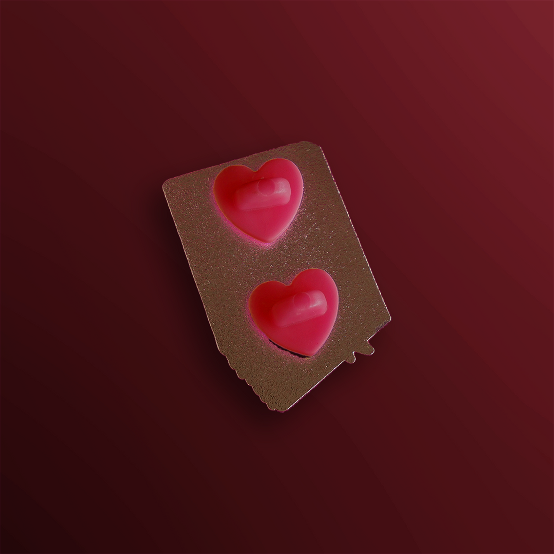 The reverse side of an enamel pin showing two backing posts with rubber red heart stoppers