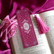 A pink bookmark with white and green accents and the text 'Slut for Smut' displayed on an open book, with a pink tassel attached.