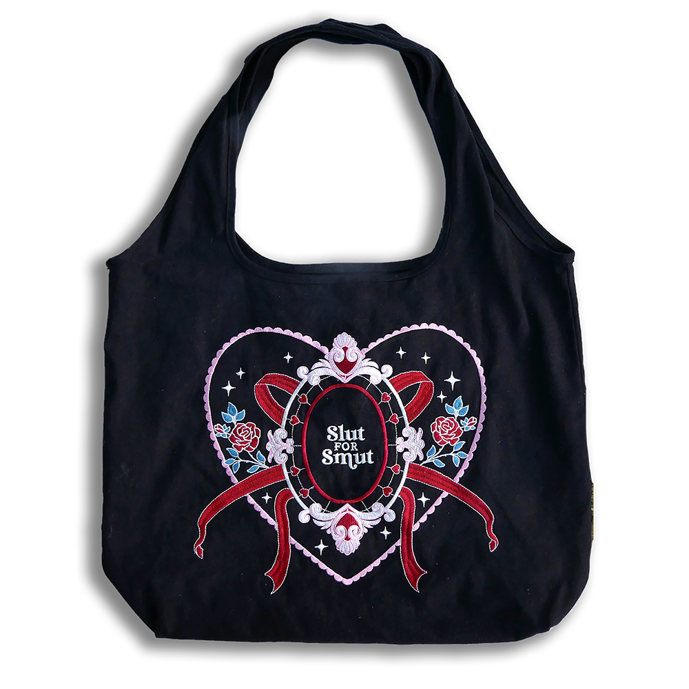 slut for smut tote bag with transparent background. Black cotton bag with red, pink, white and teal embroidery. Design features hearts, stars, leaves, scalloping and bows. 