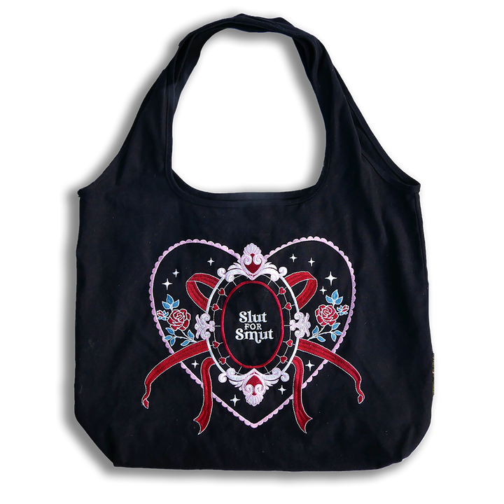 slut for smut tote bag with transparent background. Black cotton bag with red, pink, white and teal embroidery. Design features hearts, stars, leaves, scalloping and bows. 