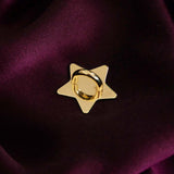 A The Quirky Cup Collective charm anchor on a dark red fabric background. The gold star-shaped clip is used to attach Charmlets to flat surfaces (such as your device).