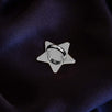 A The Quirky Cup Collective charm anchor on a dark purple fabric background. The silver star-shaped clip is used to attach Charmlets to flat surfaces (such as your device).