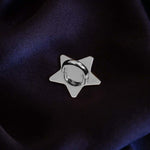 A The Quirky Cup Collective charm anchor on a dark purple fabric background. The silver star-shaped clip is used to attach Charmlets to flat surfaces (such as your device).