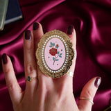 Hand holding a decorative kindle grip with a pink coquette rose inspired design with gold accents on a pink fabric background