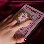 Hand holding a decorative kindle grip with a pink coquette rose inspired design with gold accents on a pink fabric background