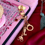Sugar & Spice eReader bundle image for romance book kindle decor- a gold charmlet with cherries, keys, a handcuff and gem is attached to an eReader with matching pink eReader sticker insert. The scene sits on a pink eReader case on red fabric.
