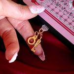 Sugar & Spice dust plug in gold shows a tiny handcuff and key being plugged into a black eReader with a pink Sugar & Spice eReader sticker insert. The hand and EReader sits on a red fabric background.

