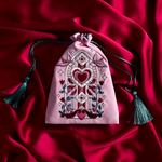 Decorative pink drawstring bag with heart and floral patterns on a red fabric background