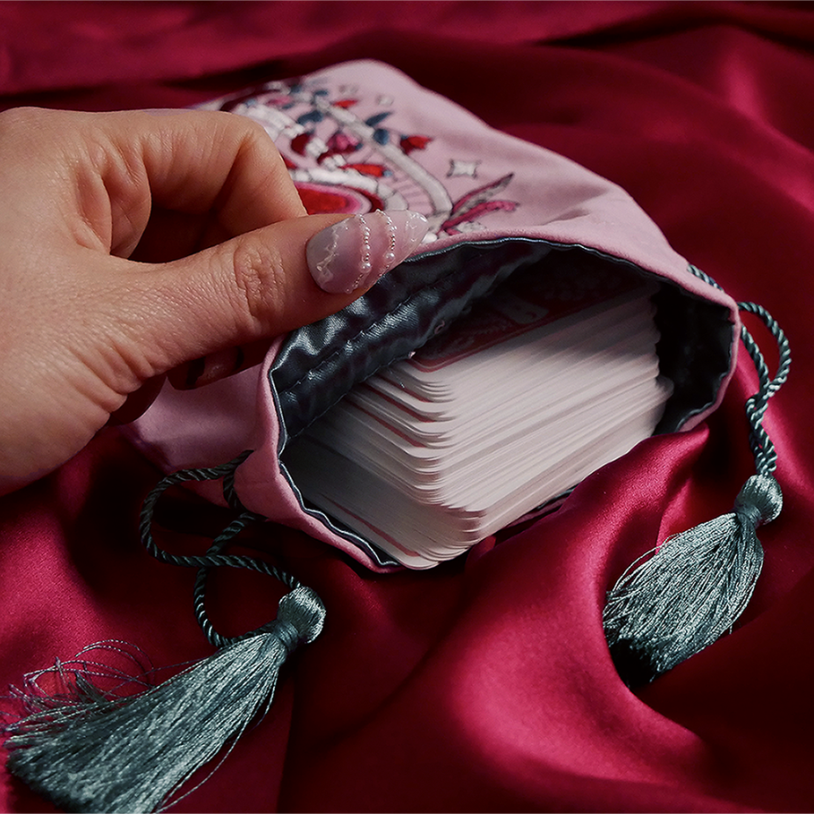 Hand holding a deck of cards in an embroidered pink case on a red fabric background