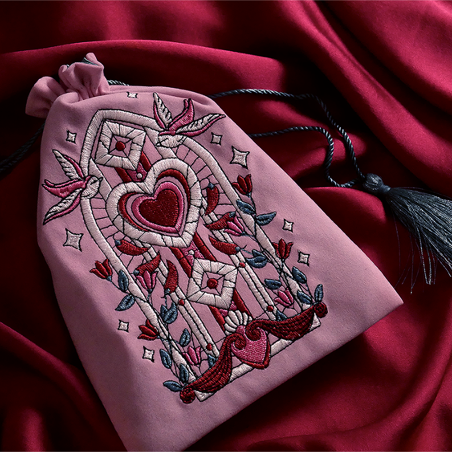 Pink drawstring bag with intricate embroidery on a red fabric background