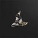 A pin shaped like a black witch's hat with gold accents and a small branch of leaves sits on a black background