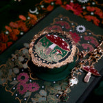 A close up of the Wonderland Kindle accessories bundle showing the embroidered eReader sleeve, decorative sticker insert and mushroom themed charmlet and MagSafe eReader grip.