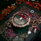 A close up of the Wonderland Kindle accessories bundle showing the embroidered eReader sleeve, decorative sticker insert and mushroom themed charmlet and MagSafe eReader grip.