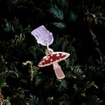 The wonderland enamel mushroom dust plug by The Quirky Cup collective sits on a bed of dark green moss.