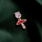 The wonderland enamel mushroom dust plug by The Quirky Cup collective sits on a dark green fabric background.