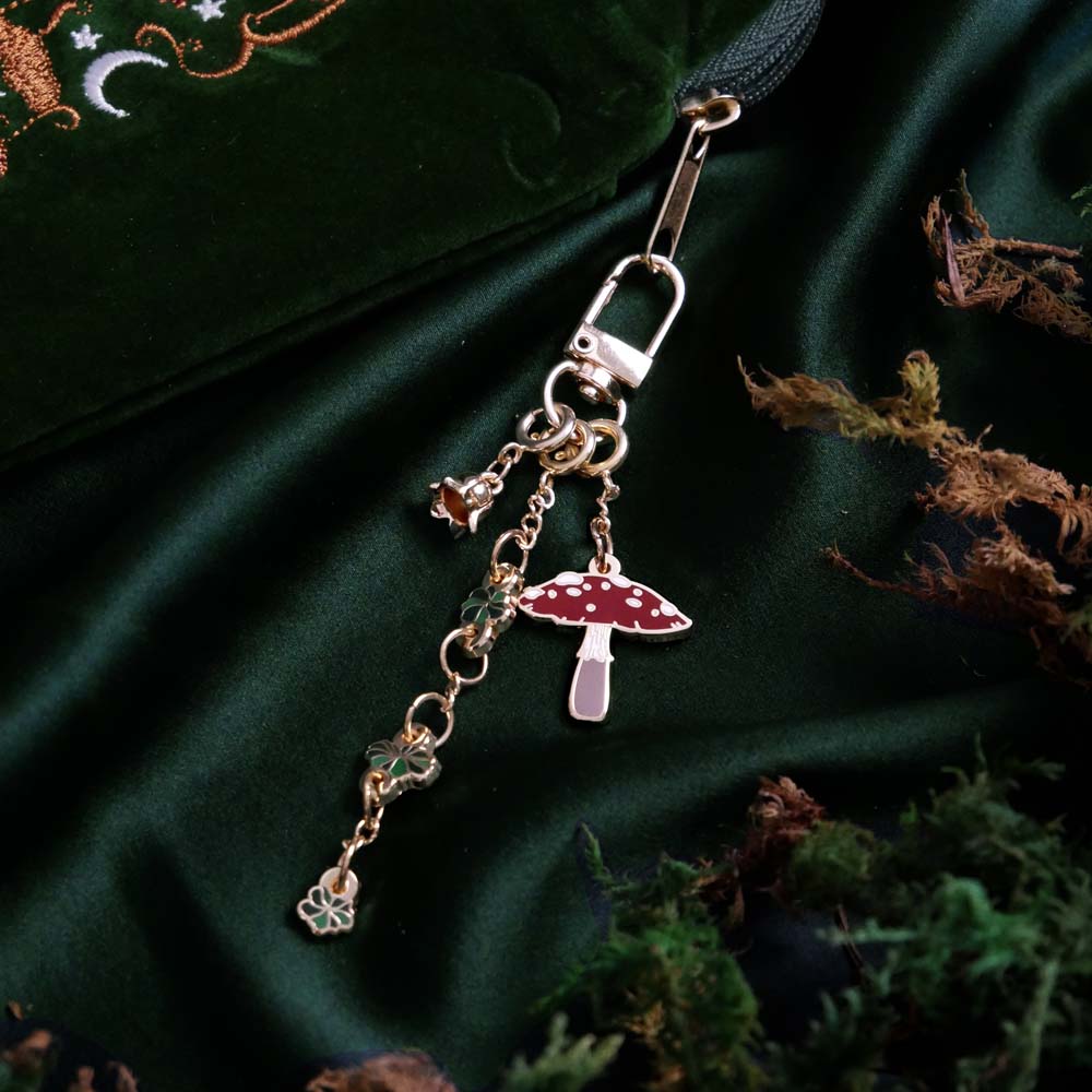 Charm keyring with mushroom charm, flower charm and leaf charm on a green fabric background attached to a kindle sleeve