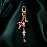 The gold Wonderland charmlet by The Quirky cup collective sits on a green fabric background. The charm features multiple other charms including a small enamel red mushroom, a chain of green leaves and a small gold flower.