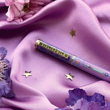 A decorative pen by The Quirky Cup Collective shows an intricate victorian inspired design and the phrase 'Bibliophile' engraved on the clip. The pen is on a purple fabric background with flowers and small gold stars.