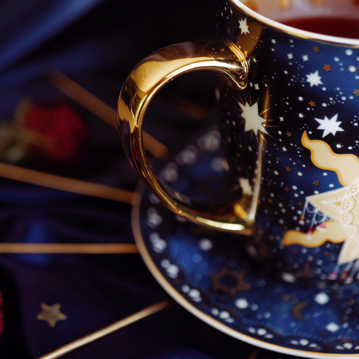 Live by the Sun Coffee Mug - Blue Mug with Gold handle and metallic gold details - Moon and Stars - Celestial Design - Le Soleil Le Gobelet - Sun Mug against satin backdrop with dried red roses and gold accessories The Quirky Cup Collective